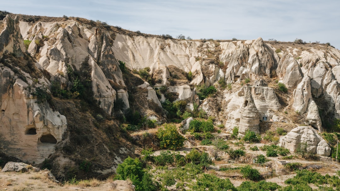 a rocky cliff with a cave with Cappadocia in the background
